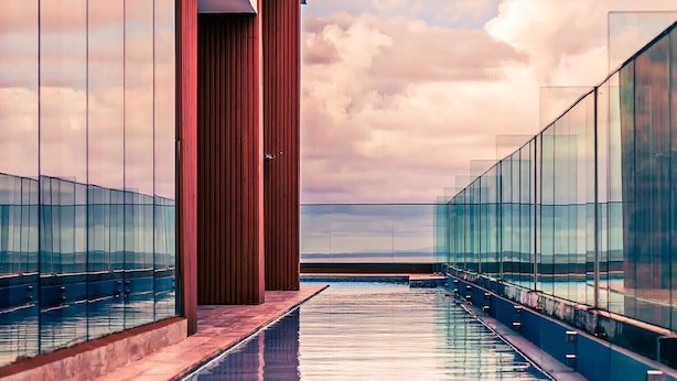 Un área de piscina moderna con barandillas de vidrio y vistas al mar.