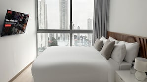 Una habitación de hotel moderna con una cama grande, una mesita de noche, una lámpara y un televisor mostrando un anuncio de Netflix.