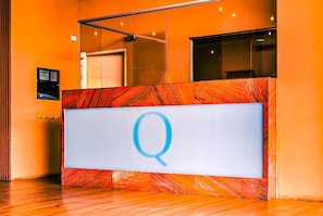 Un mostrador de recepción con diseño de mármol y un gran letrero iluminado con la letra 'Q'.