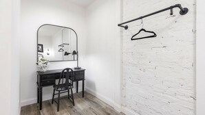 Ein Zimmer mit schwarzem Schreibtisch, Stuhl und Spiegel. Weiße Backsteinwand und Holzboden.