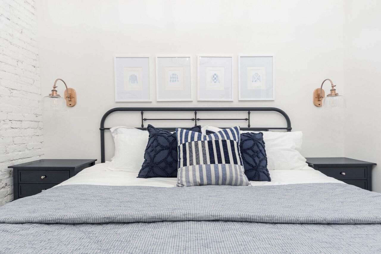 A neatly made bed with a striped blanket, a headboard with a metal frame, and two bedside tables with wall-mounted lamps.