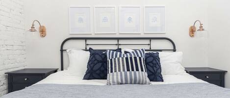 A neatly made bed with a striped blanket, a headboard with a metal frame, and two bedside tables with wall-mounted lamps.