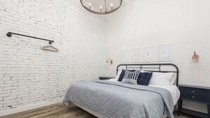 Ein Schlafzimmer mit Bett, Nachttisch, Pendelleuchte und Backsteinwand.