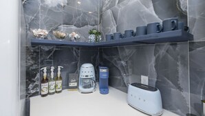 A kitchen with a marble backsplash, a toaster, a coffee maker, and a shelf with mugs and a plant.