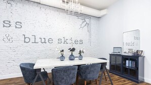 A dining area with a white brick wall, a white table, and four blue chairs.