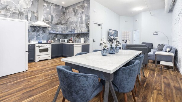 A modern kitchen with marble backsplash, a dining area with a marble table, and grey upholstered chairs.