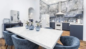 A modern kitchen with marble backsplash, white cabinets, and a dining area with a marble table and blue chairs.
