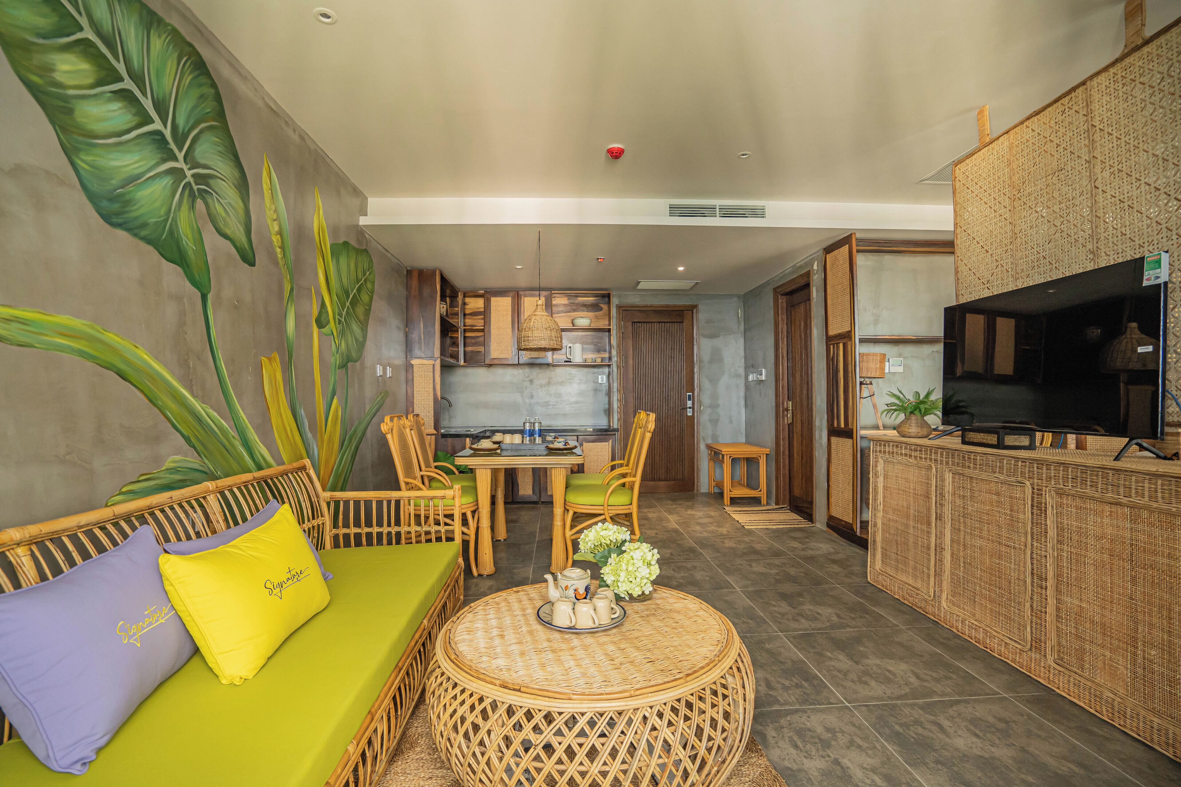 Una habitación con un sofá verde, sillones de mimbre, una mesa redonda de mimbre y un televisor sobre un mueble.
