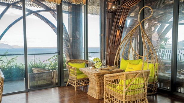 Eine Lounge-Ecke aus Rattan mit Tisch und Stühlen, großen Glasüren und Meerblick.
