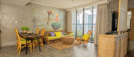 A modern living room with a dining area, a large window with a view of buildings, and a flat-screen TV on a stand.