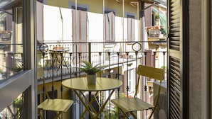 Een balkon met een tafel en stoelen, een bloempot en uitzicht op omliggende gebouwen.