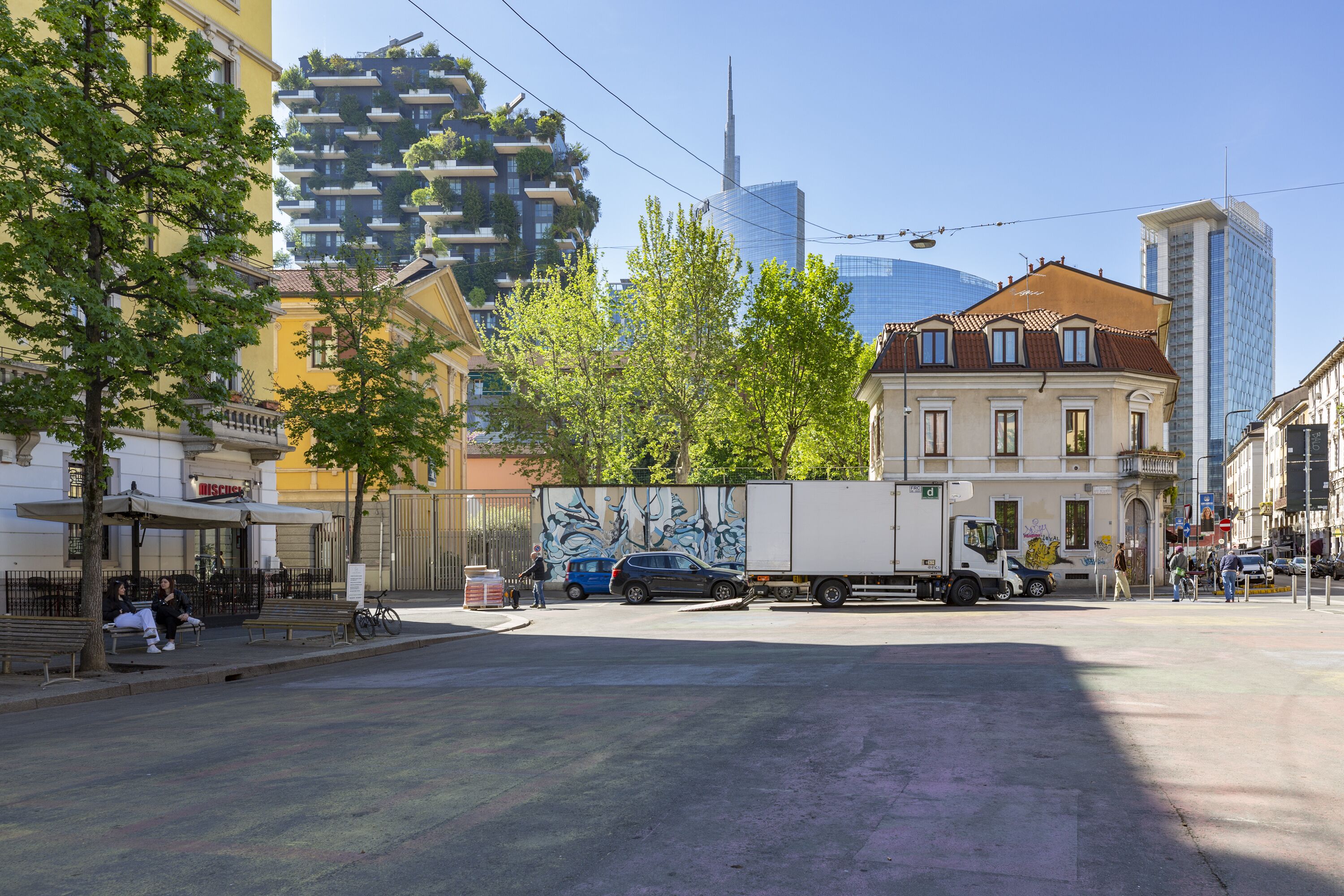 A street scene with a mix of modern and traditional buildings, a parked truck, and a few pedestrians.