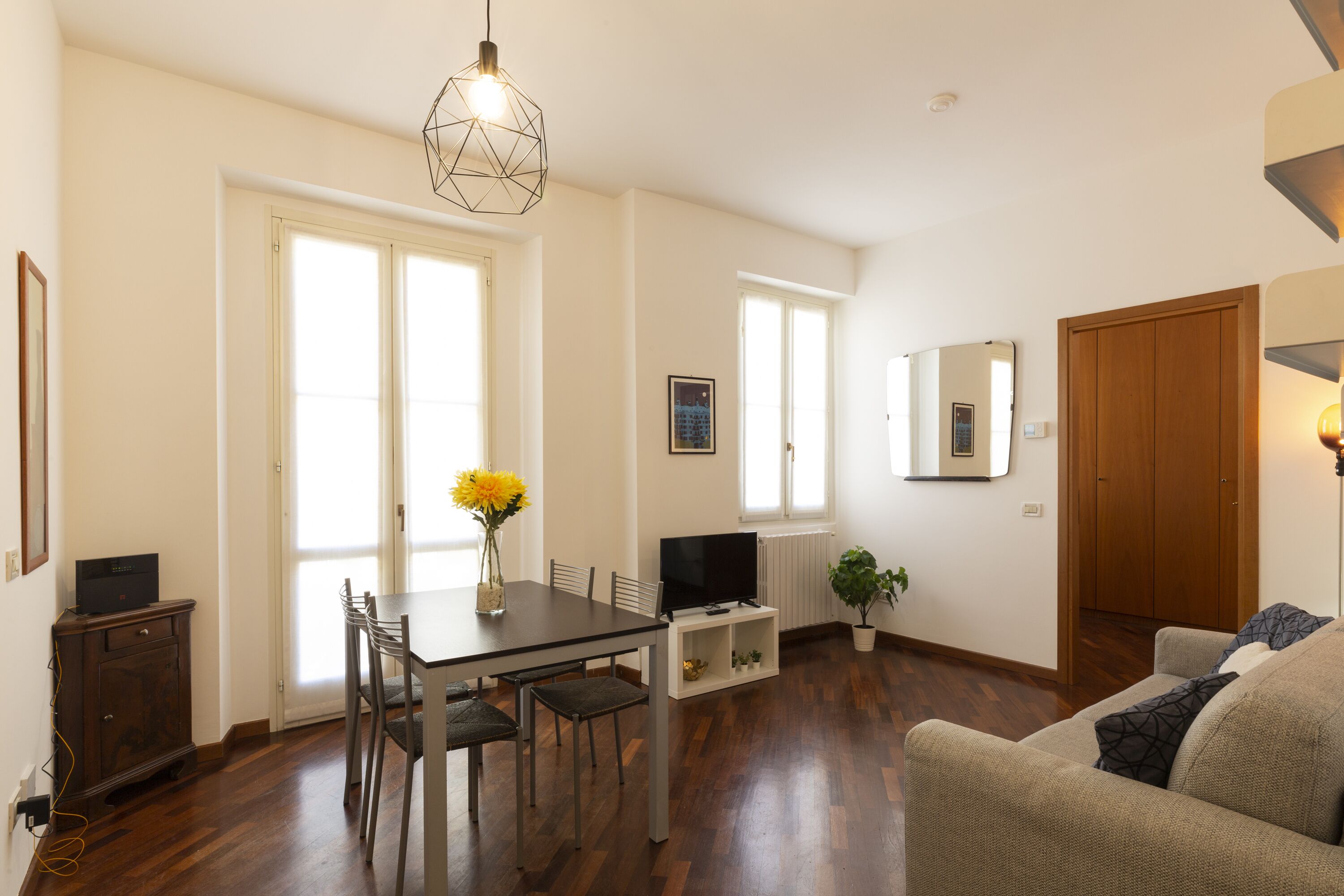 A spacious living room with a dining area, wooden flooring, and a large window providing natural light.