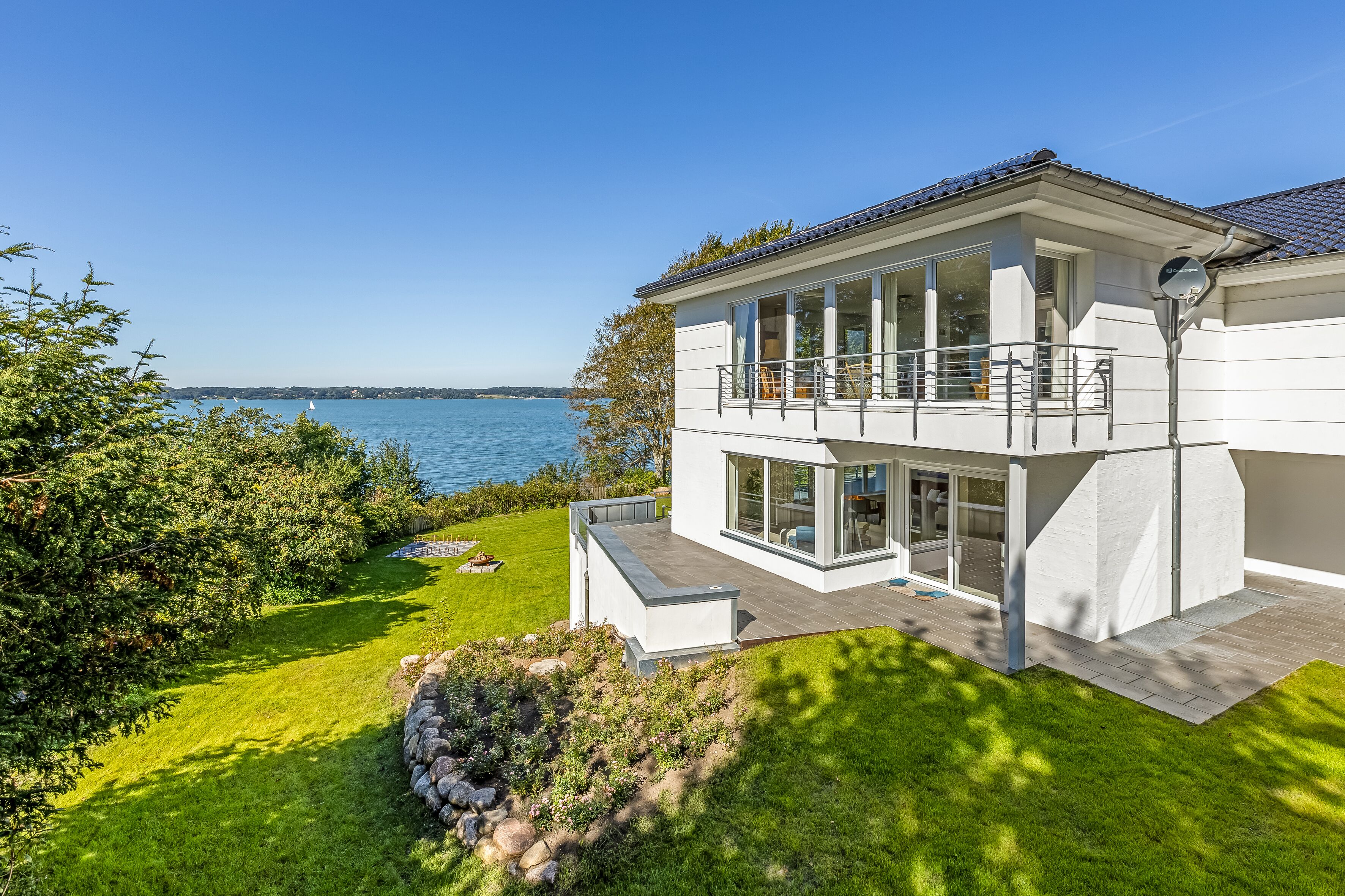 A modern two-story house with a balcony overlooking a lake.