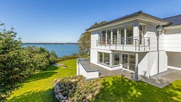 A modern two-story house with a balcony overlooking a lake.