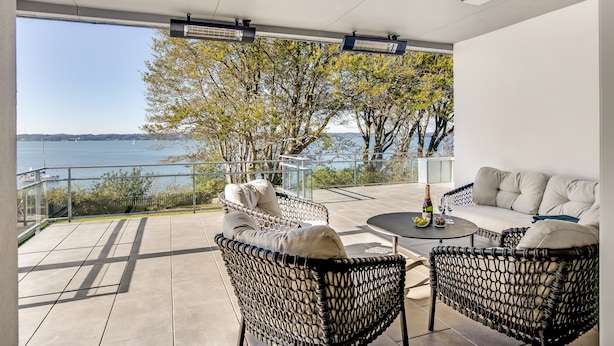 Un espacio moderno al aire libre con mobiliario de mimbre, una mesa redonda y vistas al mar.