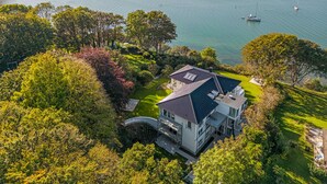 Una casa moderna con un amplio balcón que da a un lago, rodeada de abundante vegetación.