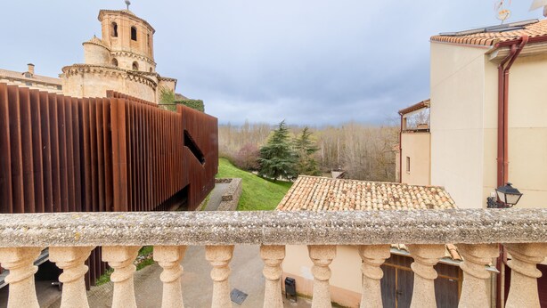 Une balustrade en pierre surplombe une cour intérieure, où se trouve un bâtiment doté d’un toit en tuiles et d’un clocher.