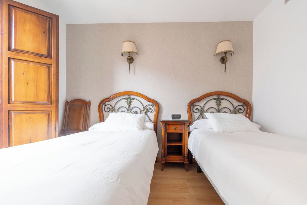 Quarto de hotel com duas camas, cabeceiras de madeira, mesas de cabeceira com luminárias e um guarda-roupa de madeira.