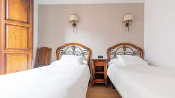 Quarto de hotel com duas camas, cabeceiras de madeira, mesas de cabeceira com luminárias e um guarda-roupa de madeira.