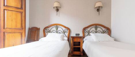 A hotel room with two beds, wooden headboards, bedside tables with lamps, and a wooden wardrobe.