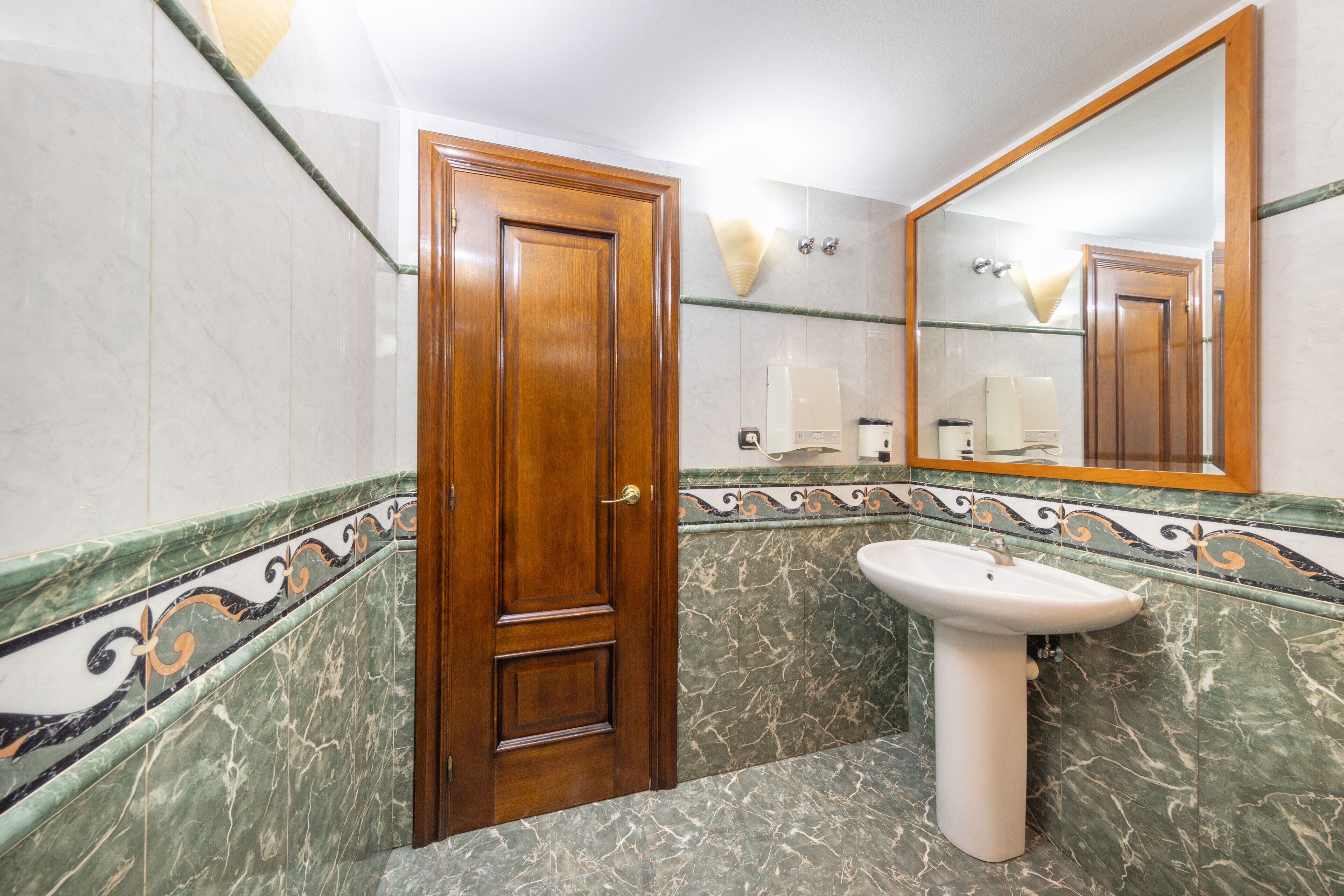 A bathroom with a wooden door, a pedestal sink, and a mirror.