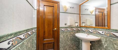 Un baño con puerta de madera, lavamanos pedestal y espejo.