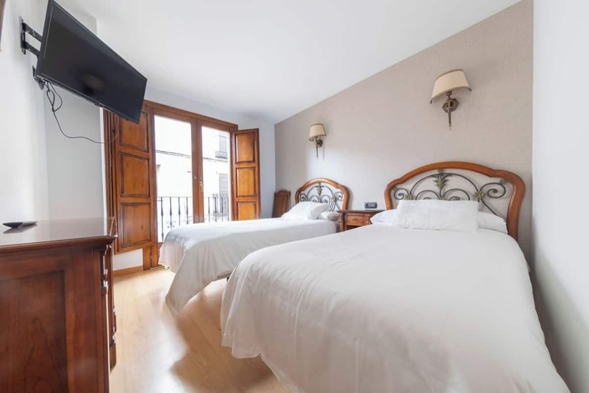 A hotel room with two beds, a TV mounted on the wall, and a balcony door.