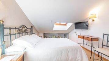 A bedroom with a bed, a desk, a chair, a TV, and a skylight.