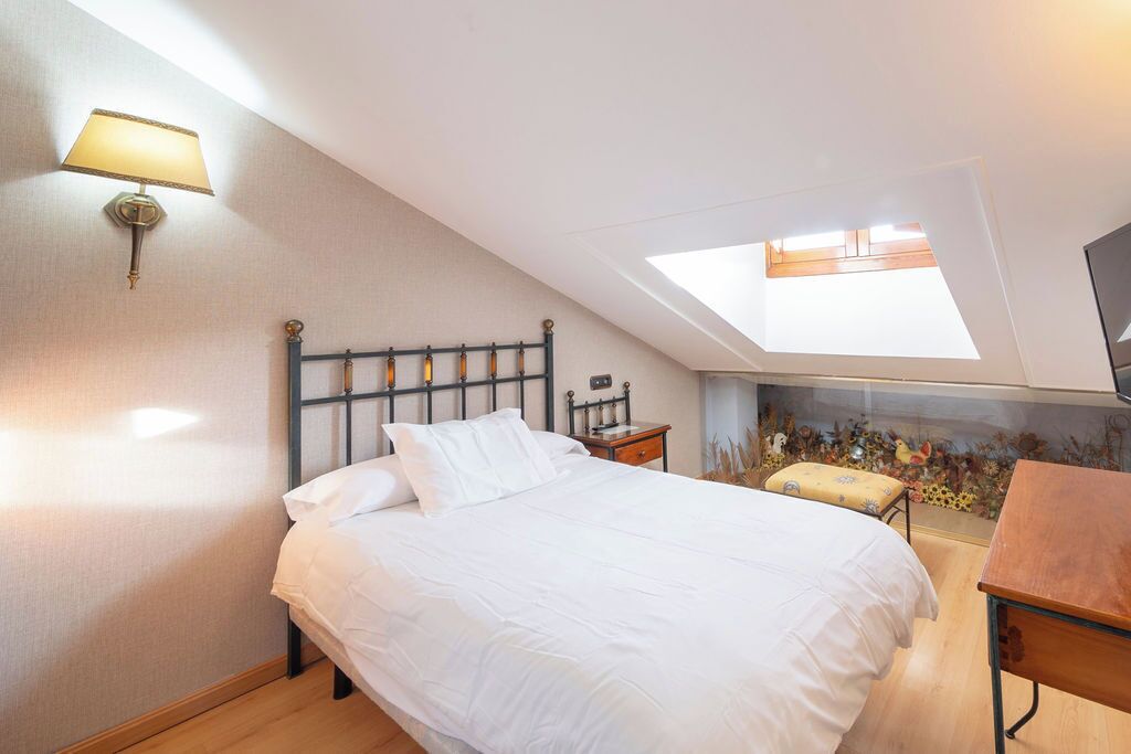 Un dormitorio con tragaluces, una cama con ropa de cama blanca, una mesita de noche y una pequeña mesa.