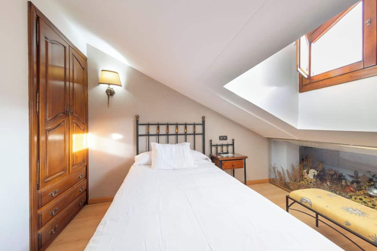 A bedroom with a bed, a nightstand, a lamp, a wardrobe, and a fish tank.
