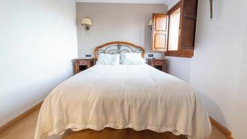 Een net opgemaakt bed met een houten hoofdbord, twee nachtkastjes en een wandlamp.
