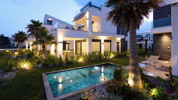 A modern multi-story house with a swimming pool, outdoor seating, and well-lit garden areas. - Olympiada Residential Complex & Villas (Pangaio)