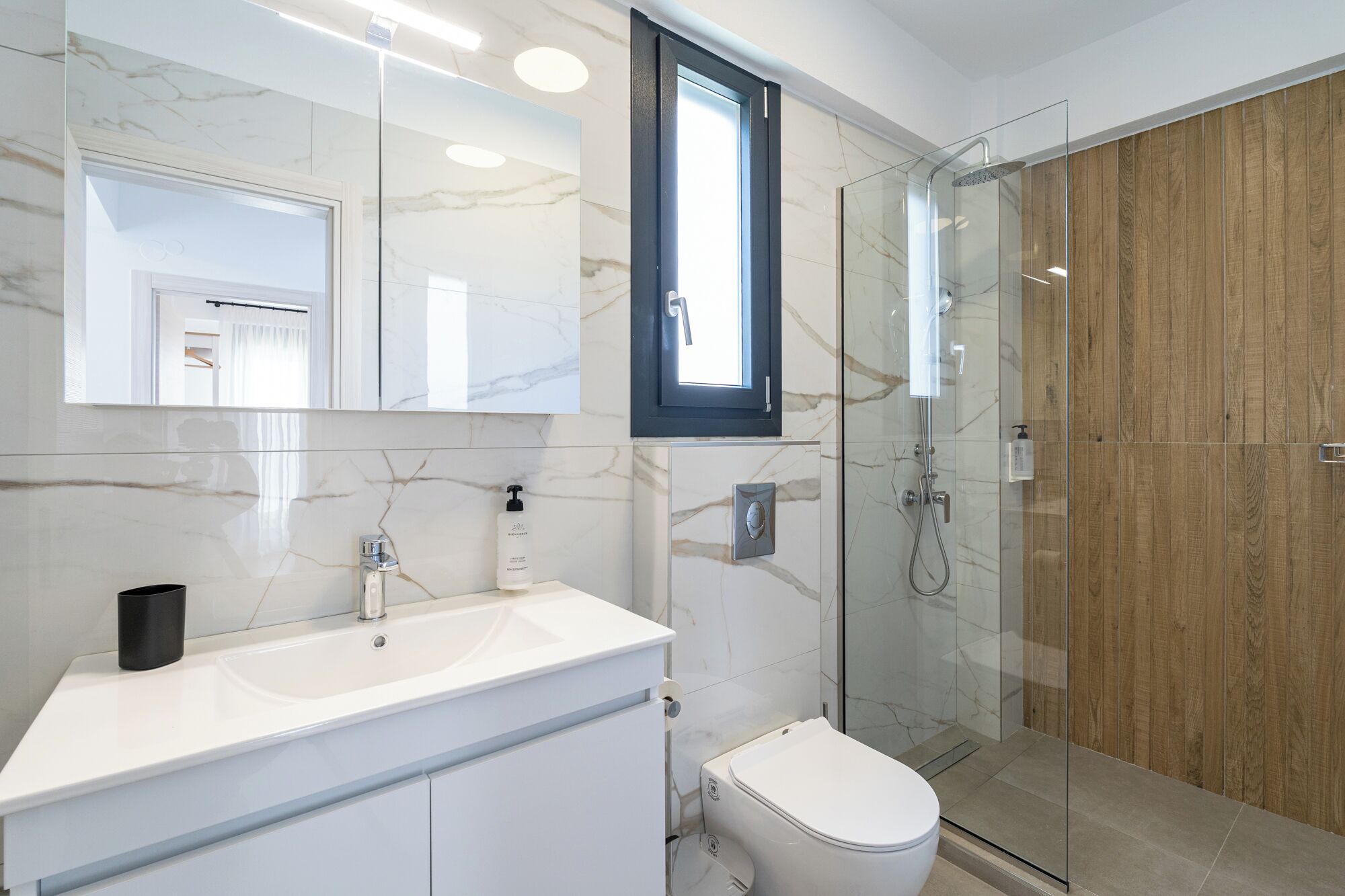 Une salle de bain moderne avec un meuble-lavabo en marbre, une cabine de douche en verre et un mur recouvert de panneaux en bois.