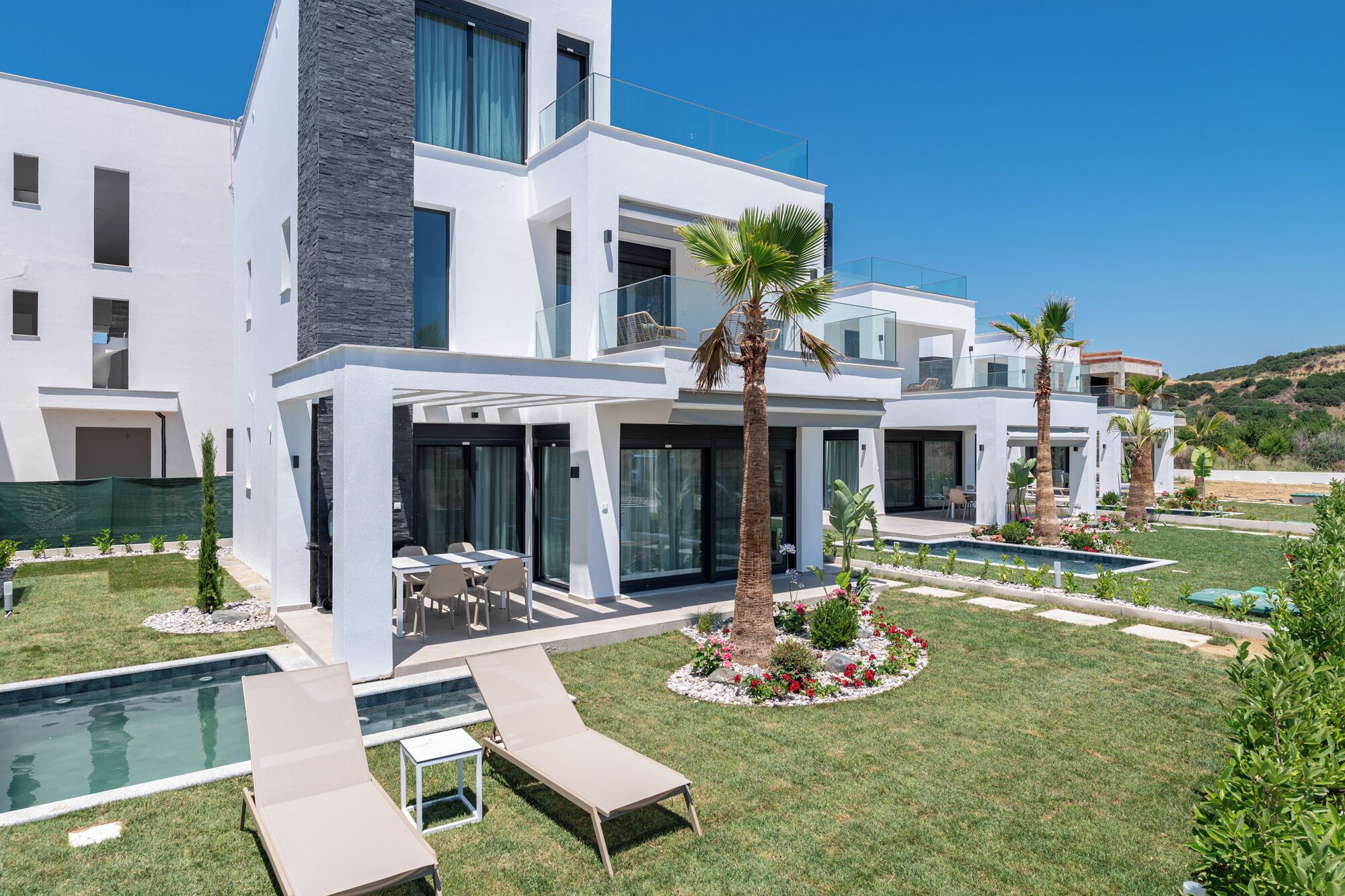 A modern two-story house with a swimming pool, outdoor seating, and a well-maintained garden.