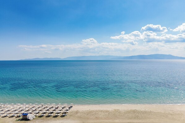 A beach with rows of umbrellas and beach chairs, a clear sky, and calm sea. - Olympiada Residential Complex & Villas (Pangaio)