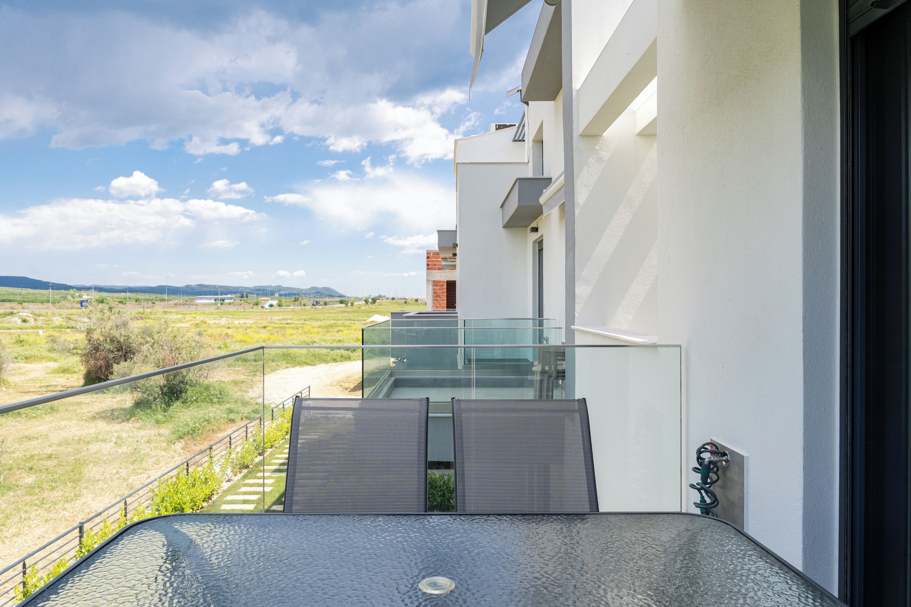 Un balcon moderne doté d’une balustrade en verre, offrant une vue sur un paysage verdoyant et des collines lointaines.