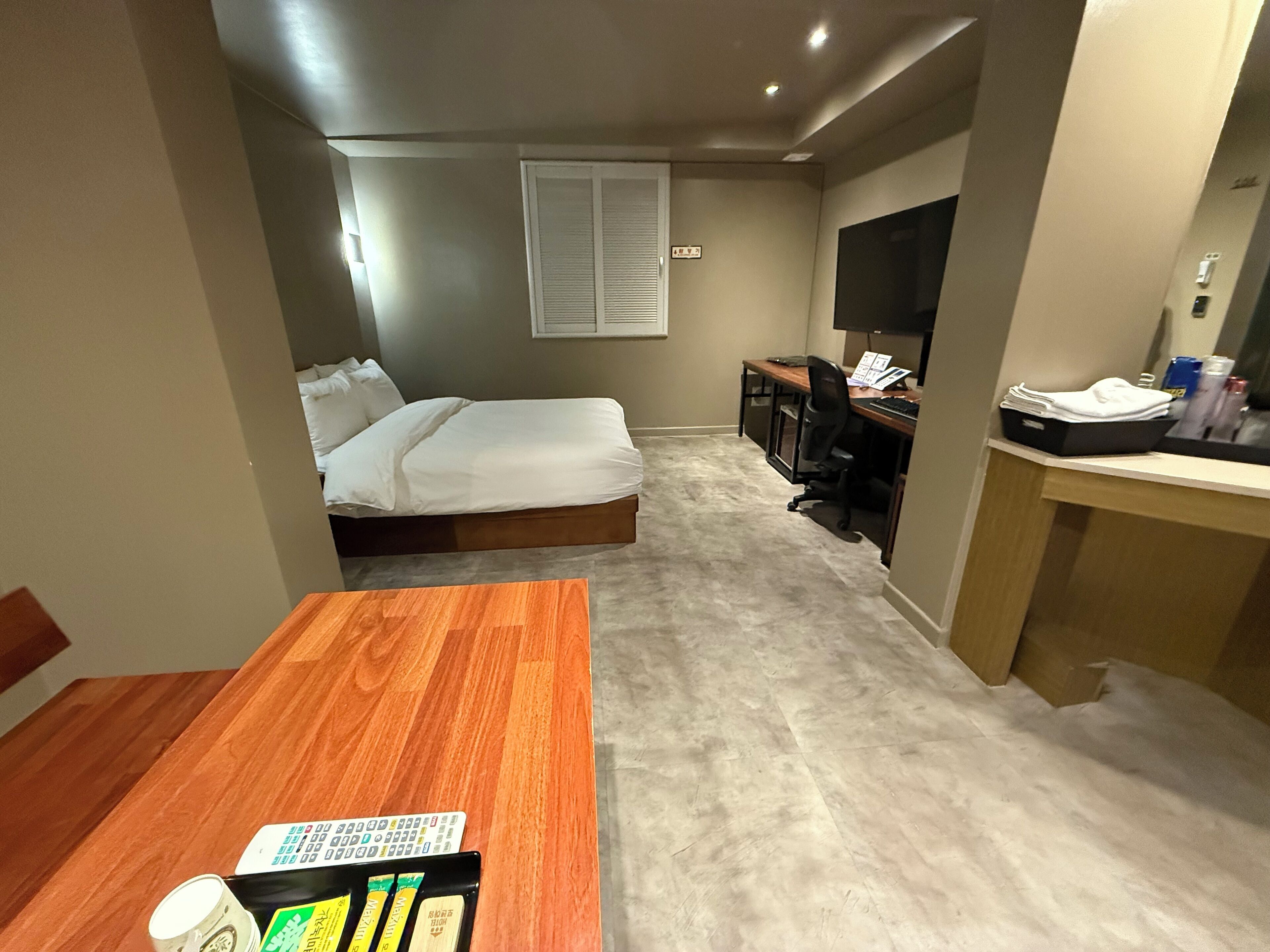 A compact hotel room with a bed, a desk, and a small seating area.