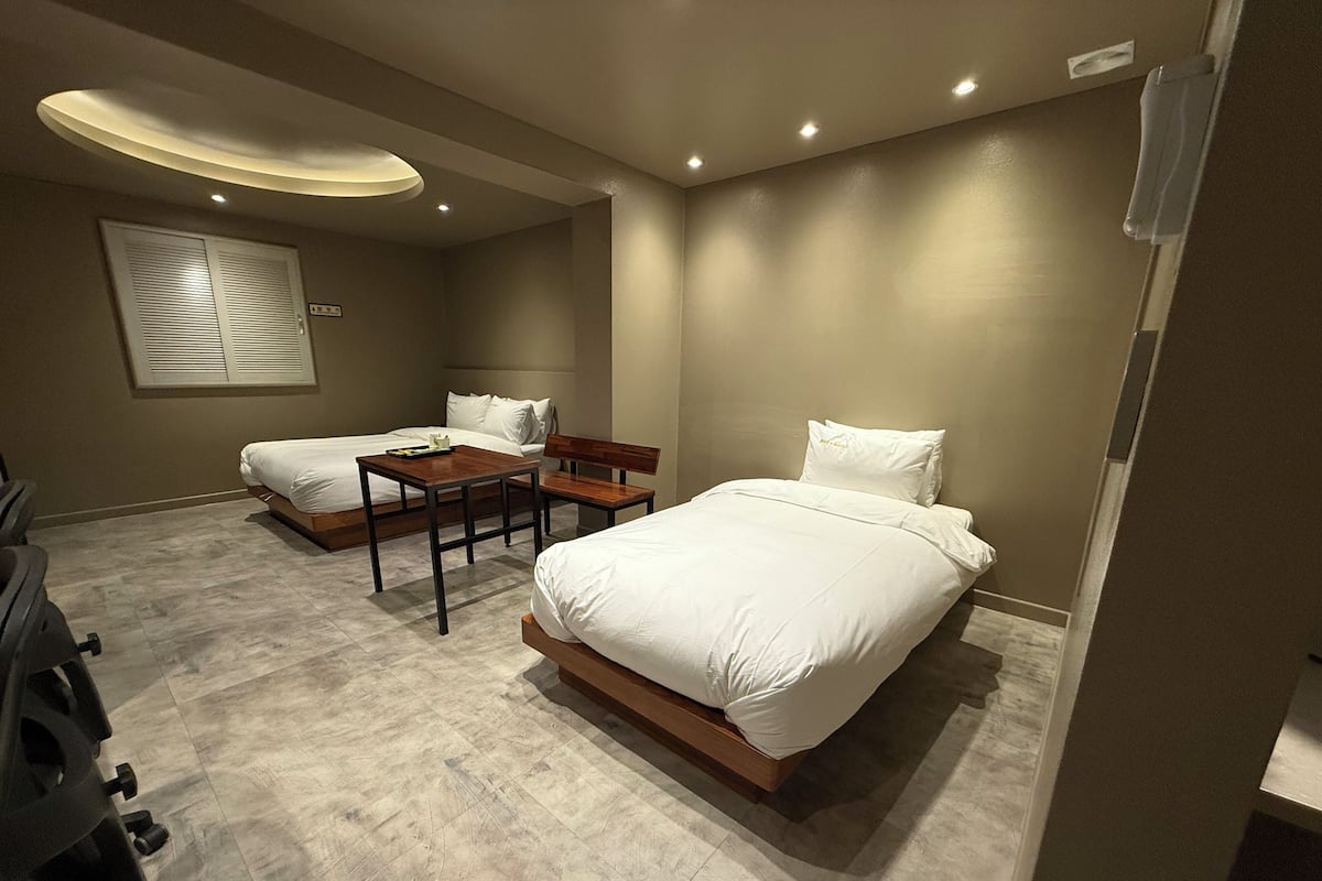Habitación de hotel con dos camas, una mesita pequeña y un banco.