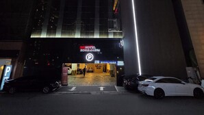 A hotel entrance with a prominent sign, a parking area, and a white car parked in front. - ROSENHEIM (Goyang)