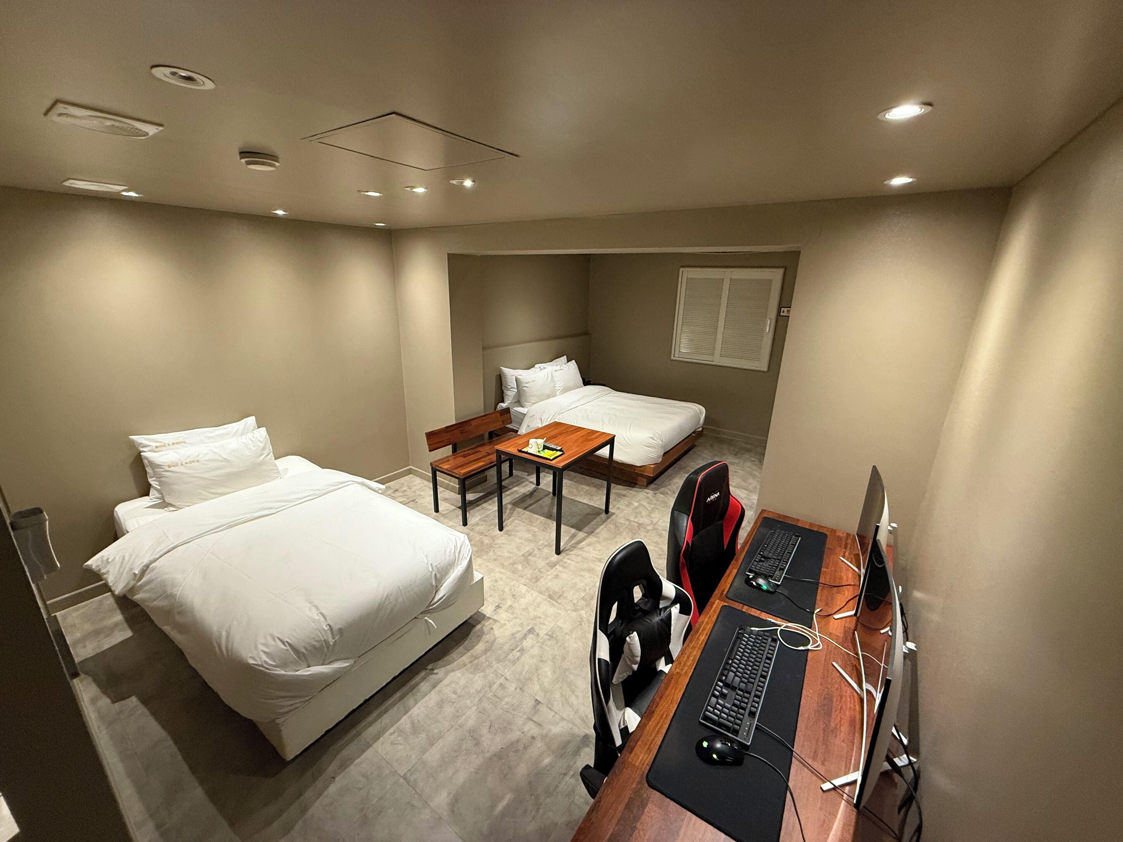A hotel room with two single beds, a desk with a computer, and a chair.