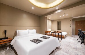 A hotel room with a large bed, a desk, a chair, and a small table.