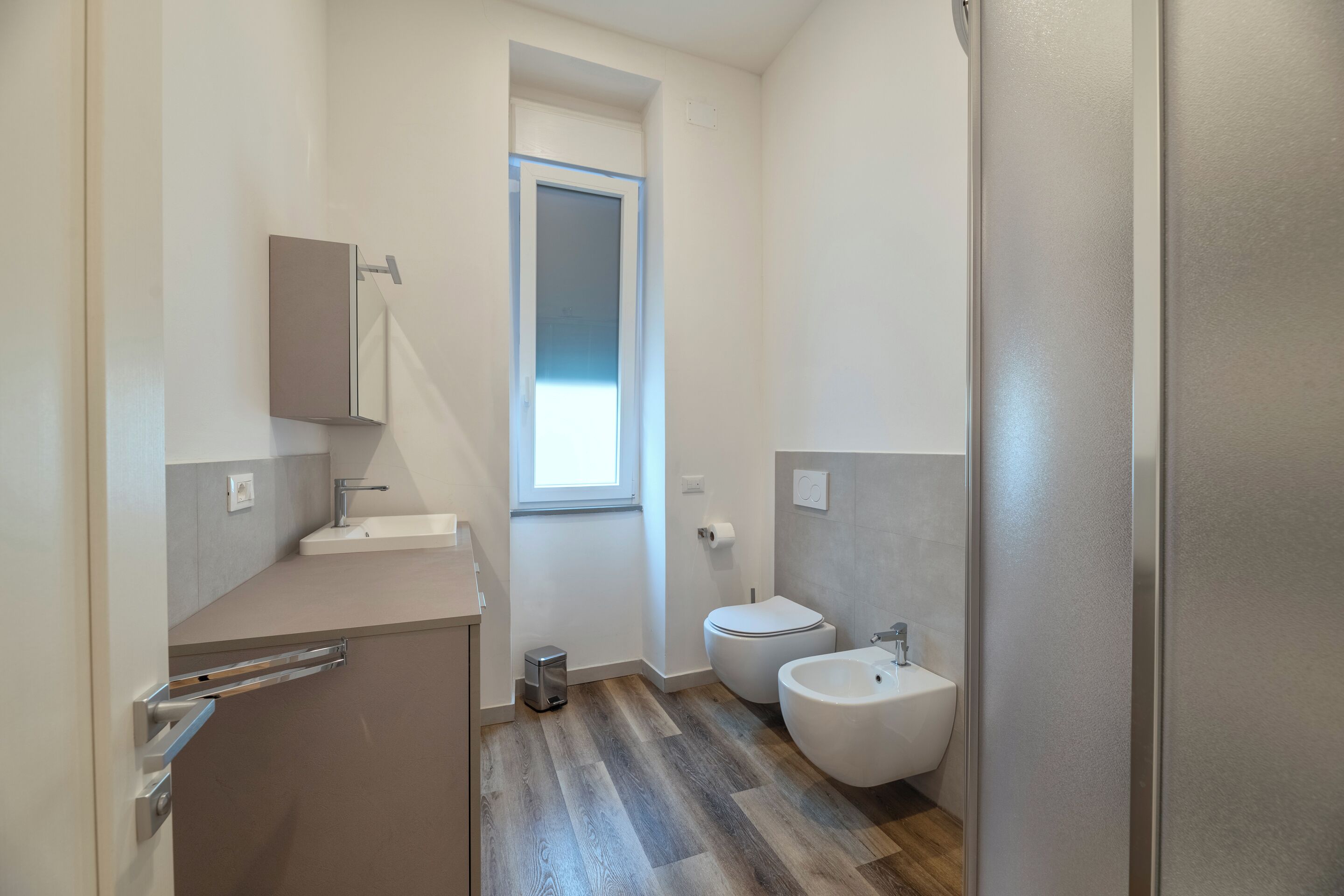 A modern bathroom with a toilet, bidet, and a small trash bin.