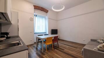 Una cocina compacta con un lavamanos, una mesa de comedor con sillas, un televisor y un sofá.