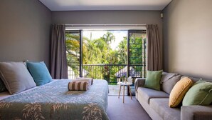 A bedroom with a bed, a sofa, and a balcony with a view of greenery. - Villa Madison | Port Douglas (PORT DOUGLAS)