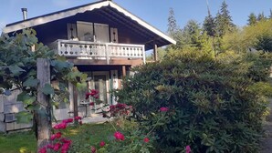Una casa con balcón, rodeada de exuberante vegetación y plantas en flor.