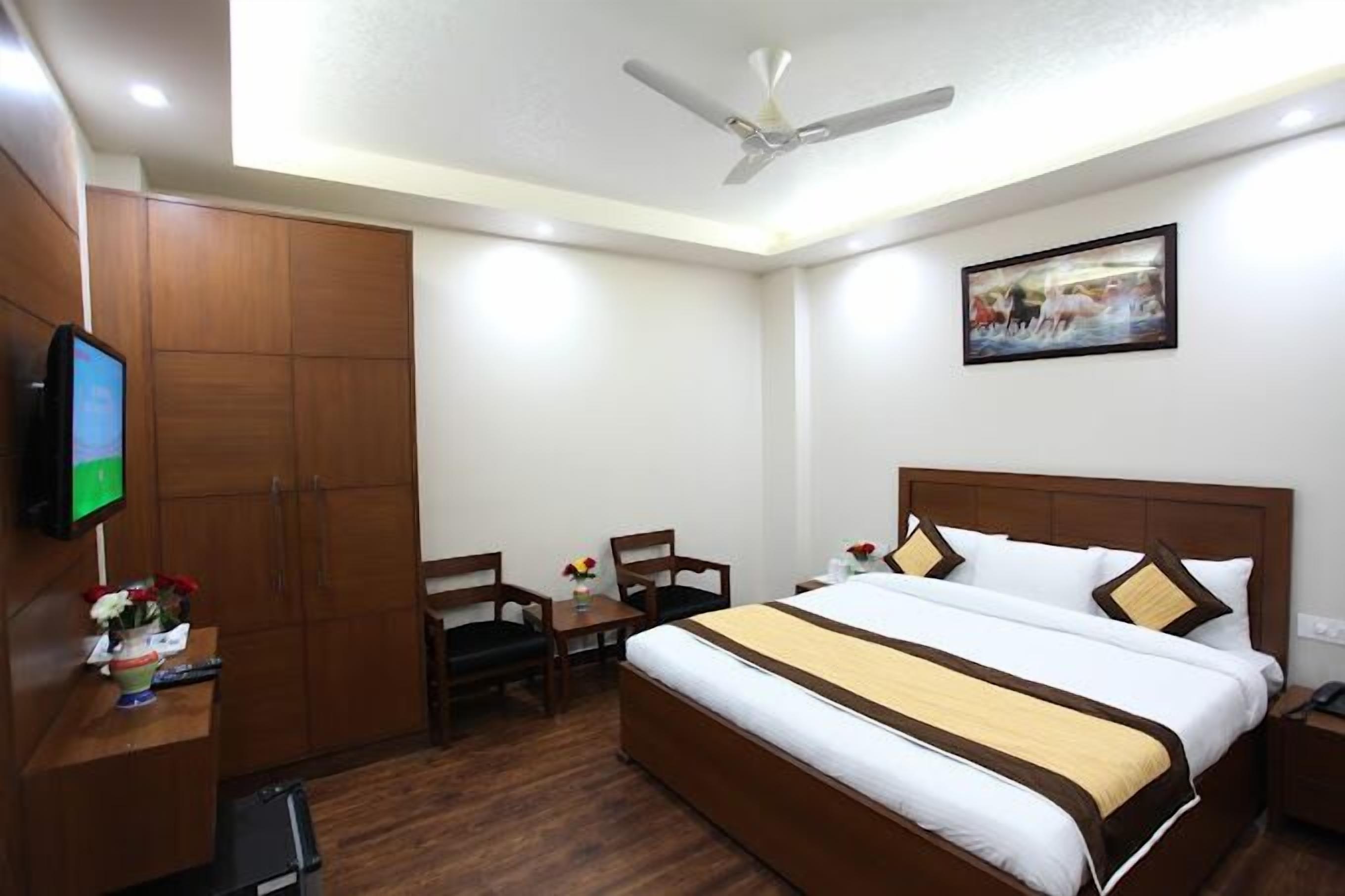 Ein Hotelzimmer mit Bett, Schreibtisch, Stuhl, Fernseher und Deckenventilator.