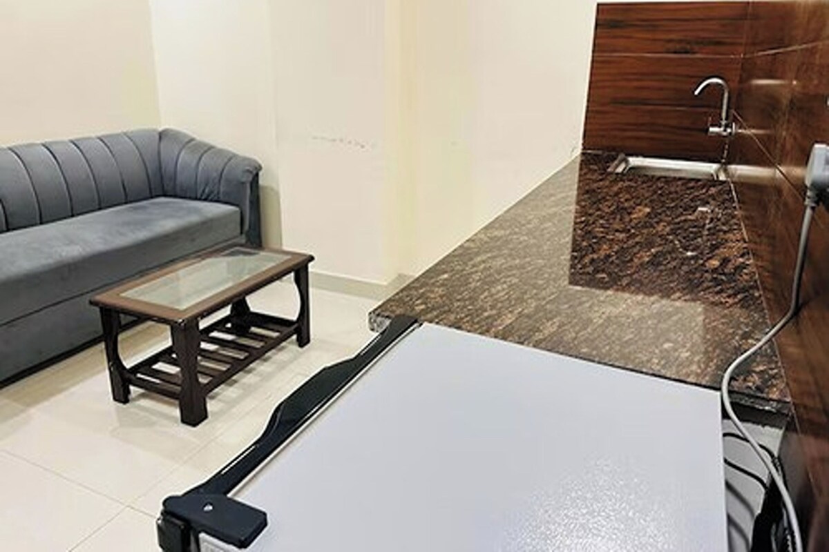 A compact living space with a grey sofa, a small wooden table, a white cabinet, and a shower area with a dark tiled floor.