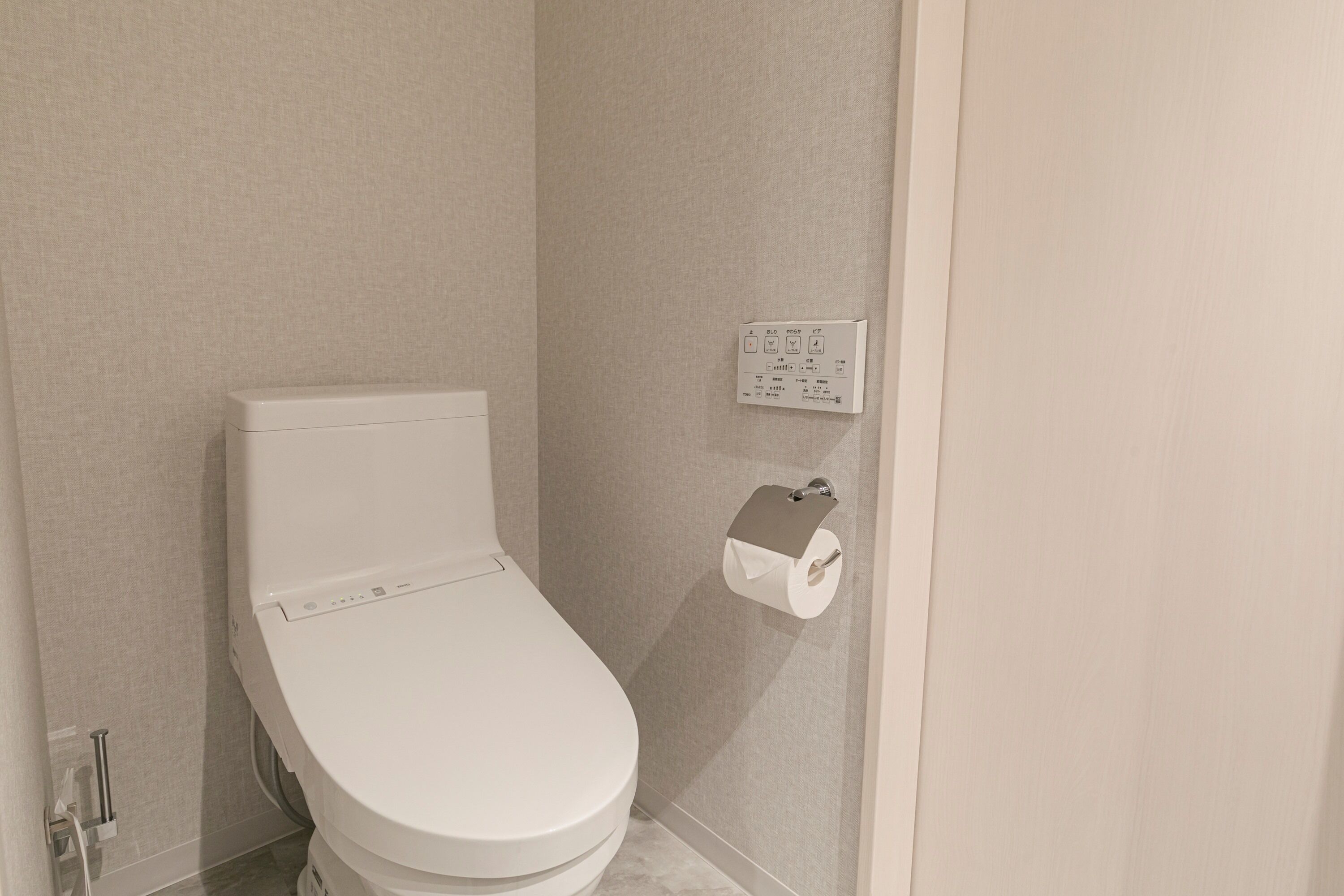 Un baño moderno con inodoro, dispensador de toallas de papel y panel de control en la pared.