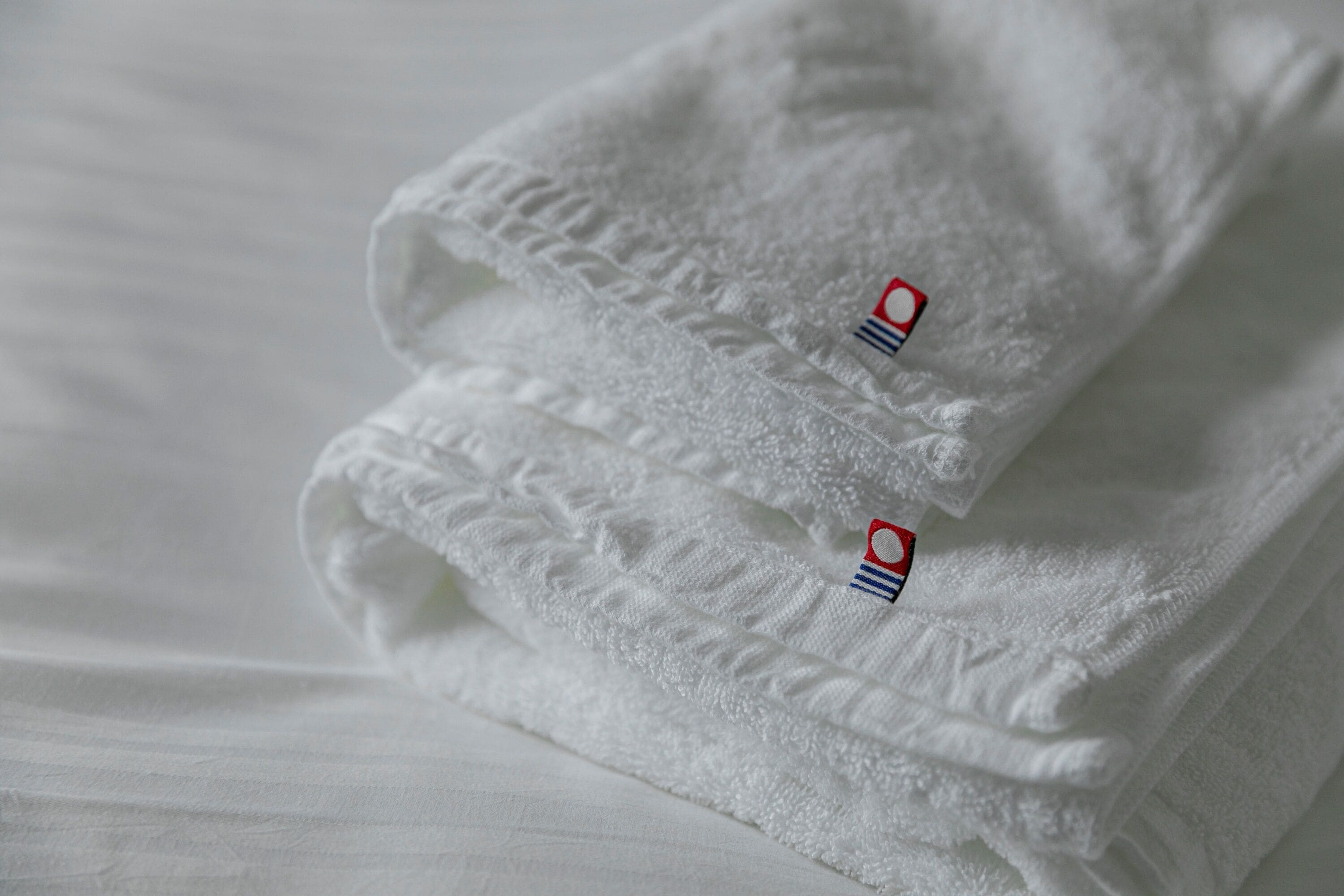 A neatly folded white towel with a small embroidered logo on the corner.